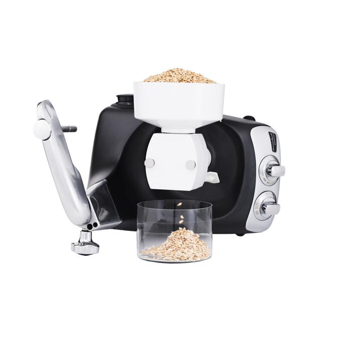 Black and silver stand mixer fitted with a white flake mill attachment rolling oats into flakes collected in a clear container, ideal for Kitchen & Food, Baking Supplies, Grain Mills, and Promo Eligible collections.