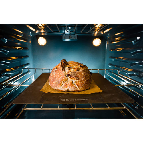 Rustic loaf baking on a dark heat-conductive steel surface in a well-lit oven, showcasing quality cookware ideal for Kitchen & Food, Baking Supplies, and Bread Making collections.