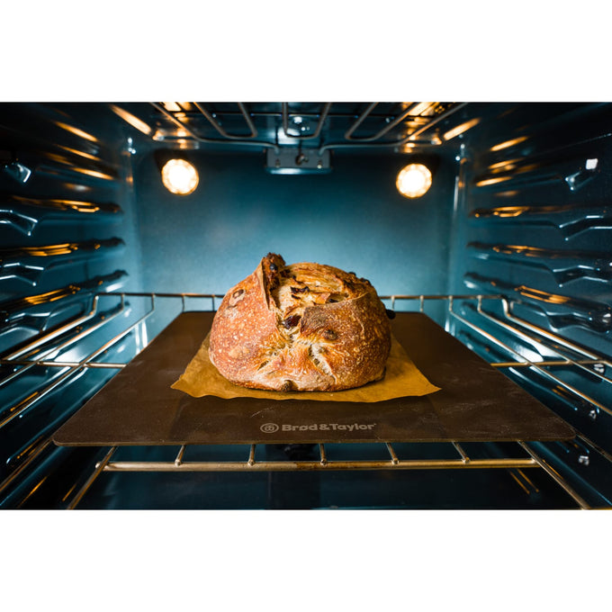 Rustic loaf baking on a dark heat-conductive steel surface in a well-lit oven, showcasing quality cookware ideal for Kitchen & Food, Baking Supplies, and Bread Making collections.
