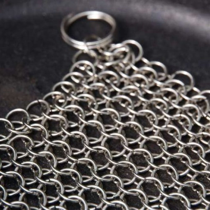 Close-up of a handcrafted stainless steel chainmail scrubber with keyring handle resting on a cast iron surface, featured in Home & Decor, Household Cleaning, Cleaning Utensils and Gadgets, Best Sellers, and Promo Eligible collections.