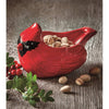 Bright red cardinal-shaped ceramic bowl holding pistachios, surrounded by green leaves and red berries, perfect for festive holiday decor and kitchen serving collections.
