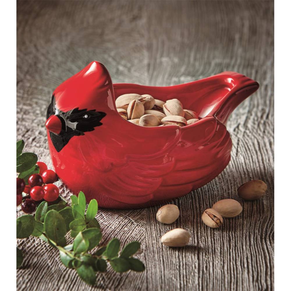 Bright red cardinal-shaped ceramic bowl holding pistachios, surrounded by green leaves and red berries, perfect for festive holiday decor and kitchen serving collections.
