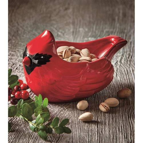 Bright red cardinal-shaped ceramic bowl holding pistachios, surrounded by green leaves and red berries, perfect for festive holiday decor and kitchen serving collections.