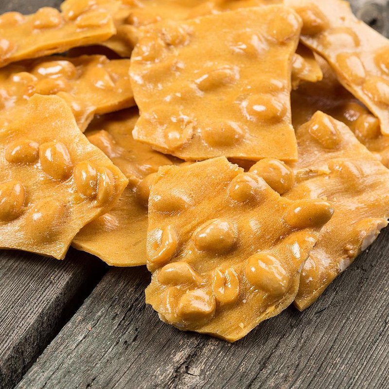 Close-up of thin, crispy peanut brittle pieces with a rich golden-butter color and whole peanuts scattered throughout, handcrafted and made in USA, ideal for Kitchen & Food and Snacks collections.
