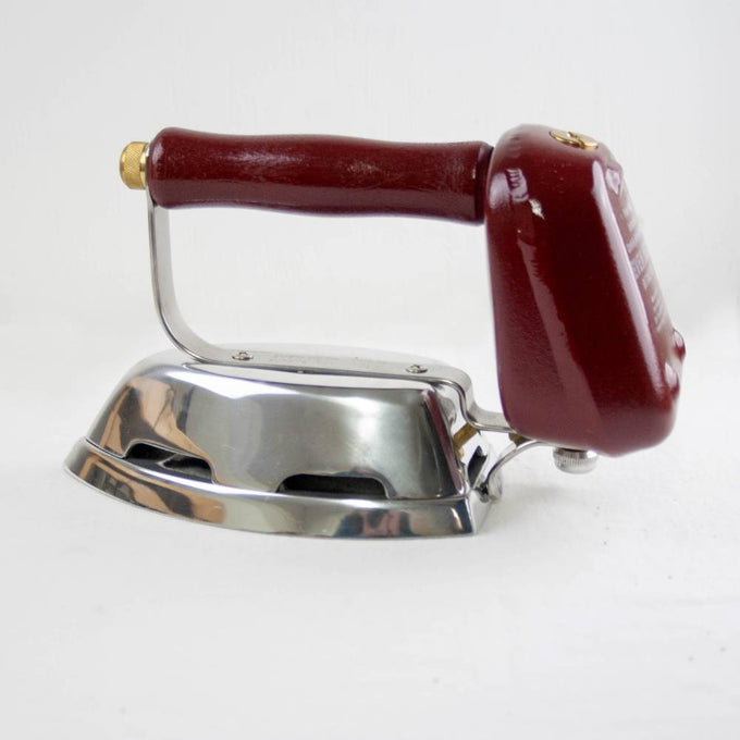 Compact butane iron with cast aluminum soleplate and polished metal finish, featuring a wooden handle and durable construction, ideal for home use and outdoor laundry tasks.