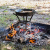 Handcrafted sturdy metal cook stand elevating a cast iron skillet over an open wood fire with glowing embers, perfect for Farm, Garden & Tool, Camping, Best Sellers, and Promo Eligible collections.