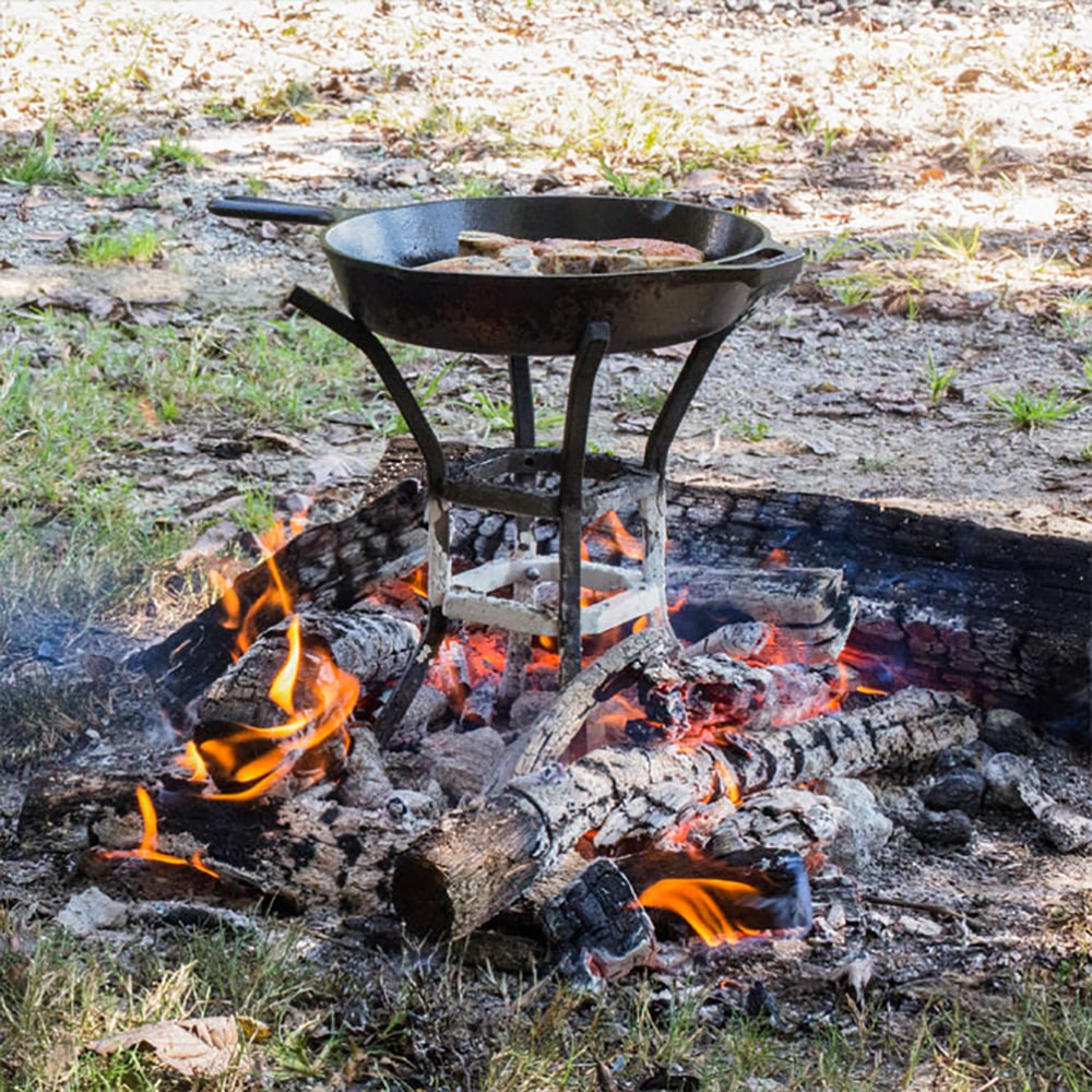 Handcrafted sturdy metal cook stand elevating a cast iron skillet over an open wood fire with glowing embers, perfect for Farm, Garden & Tool, Camping, Best Sellers, and Promo Eligible collections.