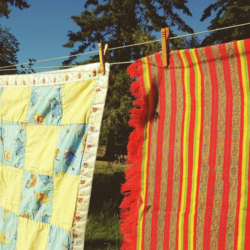 Handcrafted wooden clothespins securing a colorful quilt and a striped woven textile on a clothesline outdoors, ideal for Home & Decor and Laundry Supplies collections.