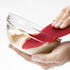 Red flexible scraper with a thin metal core, scraping batter from a clear glass bowl, designed for Kitchen & Food, Cookware, and Baking Supplies collections.
