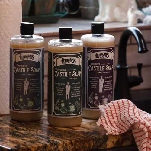 Three amber bottles of handcrafted Lehman's multi-use concentrated Castile liquid soap in unscented, peppermint, and lavender variants displayed on a kitchen countertop near a faucet and dish towel, highlighting natural USA made products in Health & Wellness, Grooming and Personal Hygiene, and Soaps collections.