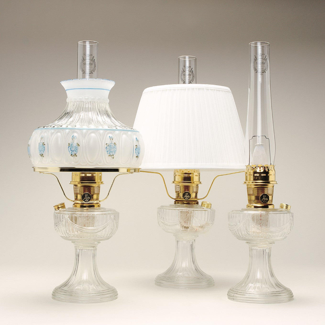 Handcrafted clear glass oil lamps featuring polished brass burners with tall chimneys, including one with a decorative painted shade, part of Lamps & Lighting, Oil Lamps, Table Lamps, Best Sellers, and Promo Eligible collections.