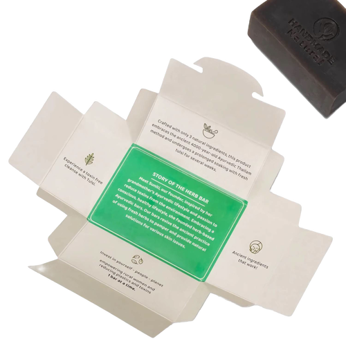 Opened packaging displaying the story and benefits of the handcrafted Tulsi Clarifying Ayurvedic Bar Soap with a dark brown bar featuring a “Handmade” impression, ideal for health and wellness and soapmaking collections.