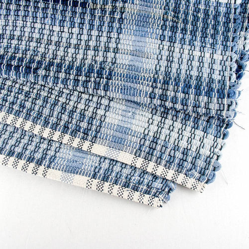 Close-up of a handcrafted woven denim rug with a textured blue pattern and finished edge, made in the USA, featured in Home & Decor and Best Sellers collections.