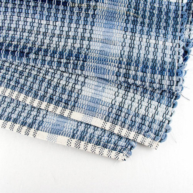 Close-up of a handcrafted woven denim rug with a textured blue pattern and finished edge, made in the USA, featured in Home & Decor and Best Sellers collections.