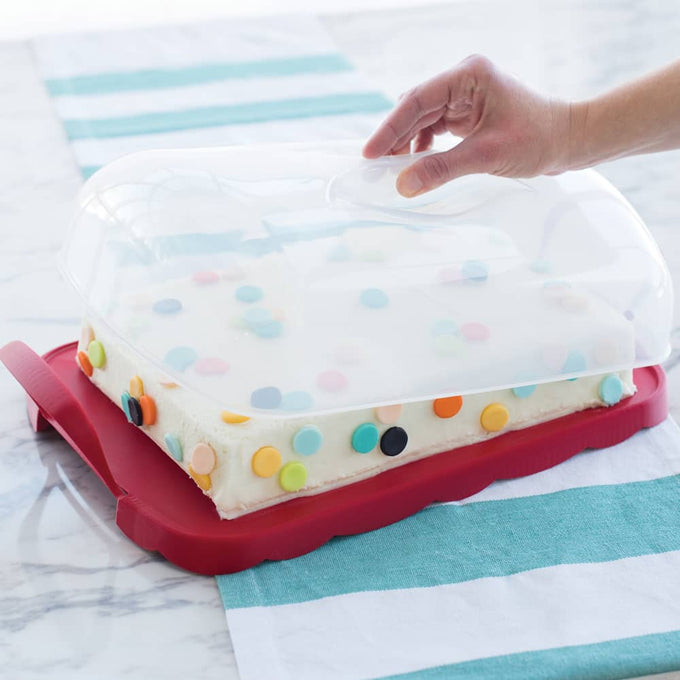 Clear domed reversible carrier with scalloped red edges and snap-lock handles, holding a rectangular cake decorated with colorful round confetti, suitable for Kitchen & Food and Baking Supplies collections.