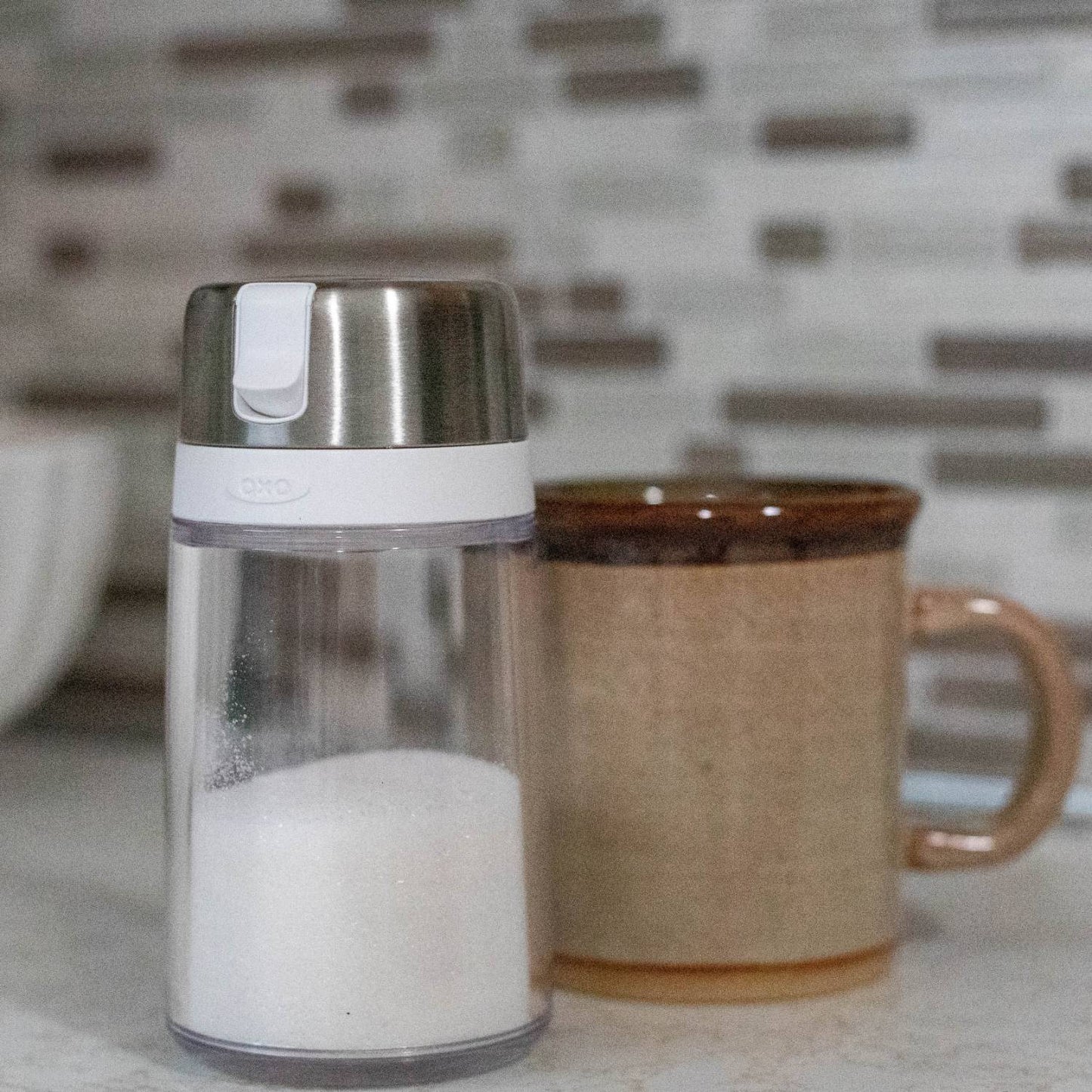 Clear glass sugar dispenser with stainless steel lid and white plastic flip-top spout, designed to minimize moisture and clumping, featured in Kitchen & Food, Kitchen Gadgets, Storage and Serving, Best Sellers, and Promo Eligible collections.