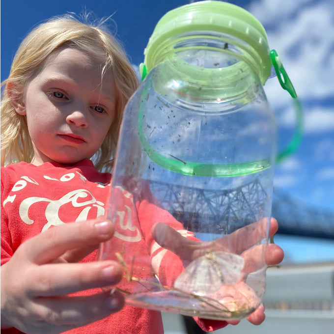 Young child outdoors holding a handcrafted clear plastic bug catcher with green magnifying cap, exploring insects as part of USA Made, Outdoor Play, and Children's Toys collections.
