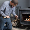 Man kneeling while using a handcrafted powder-coated steel fire tool with brass mouthpiece to tend logs inside a cast iron stove, ideal for Hearth Accessories and Stoves collections