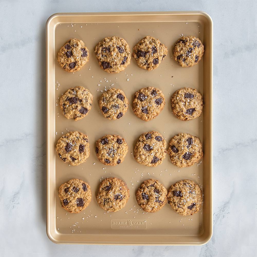 Natural aluminum baking sheet with premium gold nonstick coating, holding sixteen freshly baked chocolate chip cookies sprinkled with sea salt, ideal for Kitchen & Food, Cookware, Baking Supplies, USA Made, Best Sellers, and Promo Eligible collections.