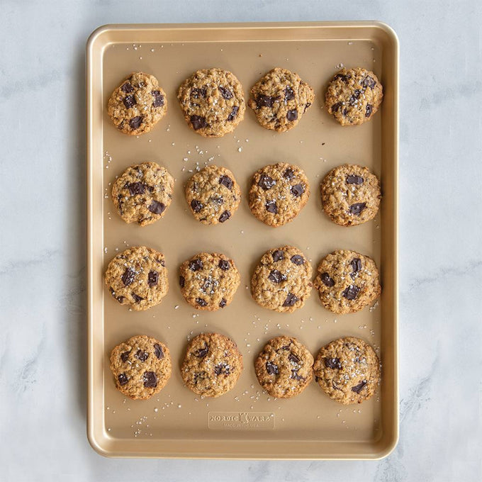 Natural aluminum baking sheet with premium gold nonstick coating, holding sixteen freshly baked chocolate chip cookies sprinkled with sea salt, ideal for Kitchen & Food, Cookware, Baking Supplies, USA Made, Best Sellers, and Promo Eligible collections.