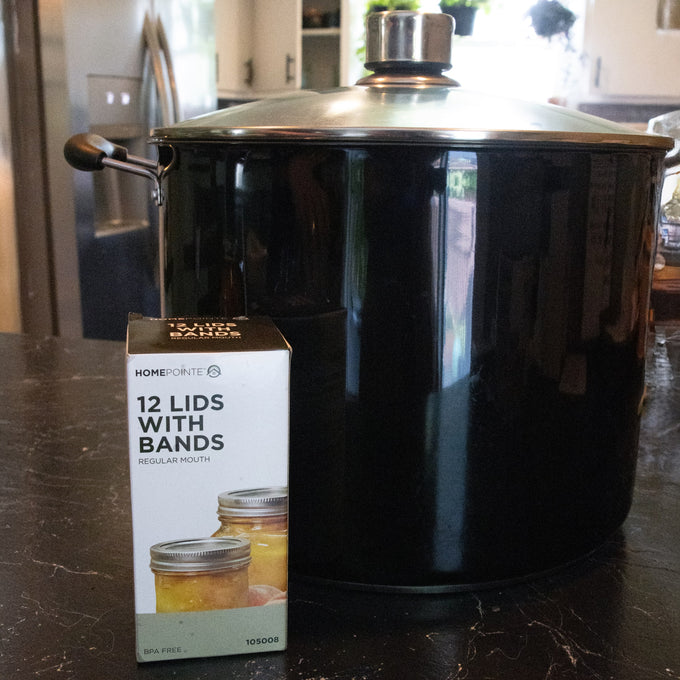Box of 12 regular-mouth canning jar lids with BPA-free sealing compound and matching bands shown on a kitchen counter next to a large black stockpot, ideal for Food Preservation and Canning collections.