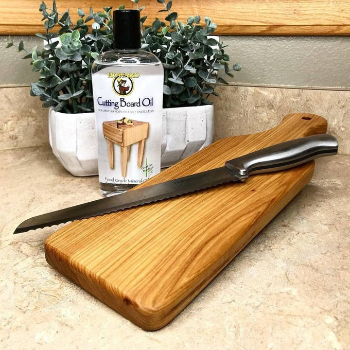 Bottle of clear food-grade mineral oil for conditioning cutting boards, shown next to a wooden cutting board and bread knife, fitting Kitchen & Food and USA Made collections.