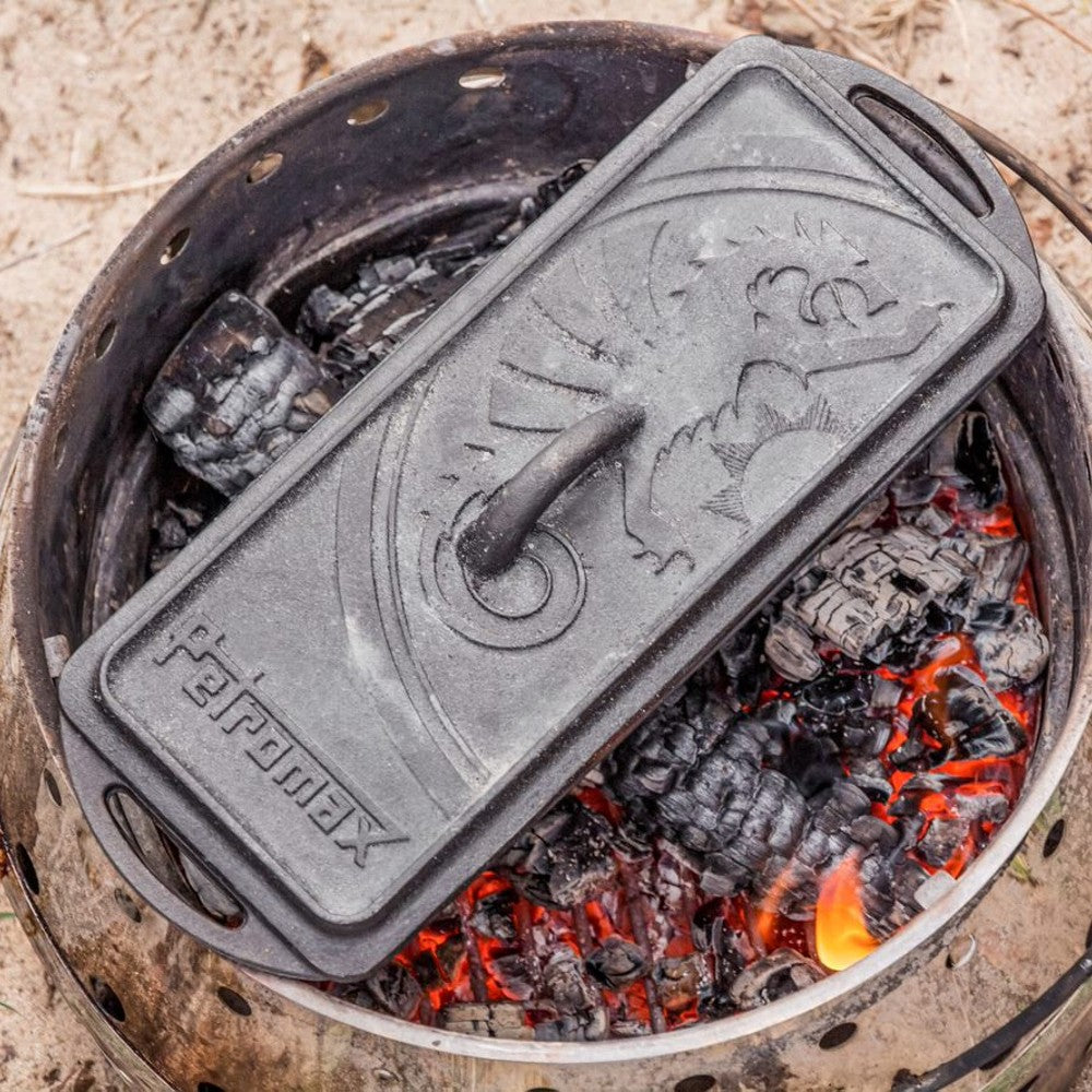 Cast iron loaf pan with embossed design cooking over glowing campfire coals, ideal for outdoor baking in Camping, Farm, Garden & Tool, and Bread Making Supplies collections.