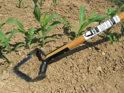 Push-pull hoe with a long ash handle and serrated hardened steel blade, handcrafted in the USA, used for cultivating soil and removing weeds in farm and garden settings.