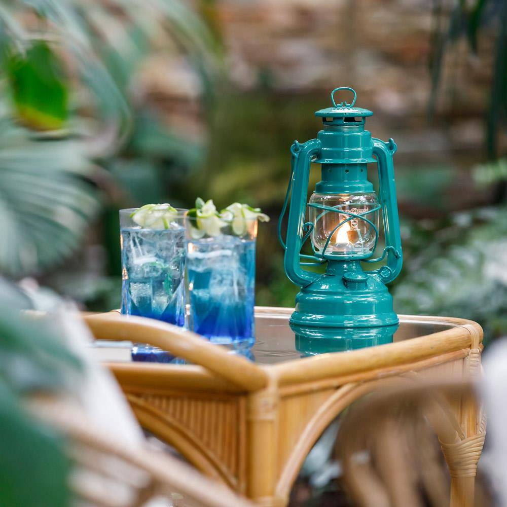 Handcrafted teal galvanized oil lantern with thermal heat-resistant globe softly glowing on a wicker table alongside two blue cocktails, perfect for Camping, Lamps & Lighting, and Emergency Supplies collections.