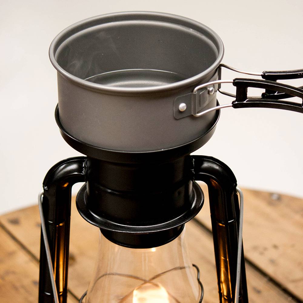 Close-up of a handcrafted black powder-coated steel lantern with a compact metal pot on top, showcasing the cooking and heating function for camping and emergency use in outdoor collections.