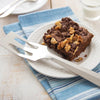 Stainless steel kitchen tool spatula with angled slotted head resting beside a walnut and chocolate chip brownie on a white plate, set on blue striped linen, showcasing USA made best seller from Kitchen & Food and Storage collections.