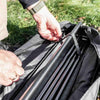 Hands securing black fire bridge poles inside a durable ripstop transport bag with reinforced zipper and strap, designed for farm, garden, camping, and outdoor use.