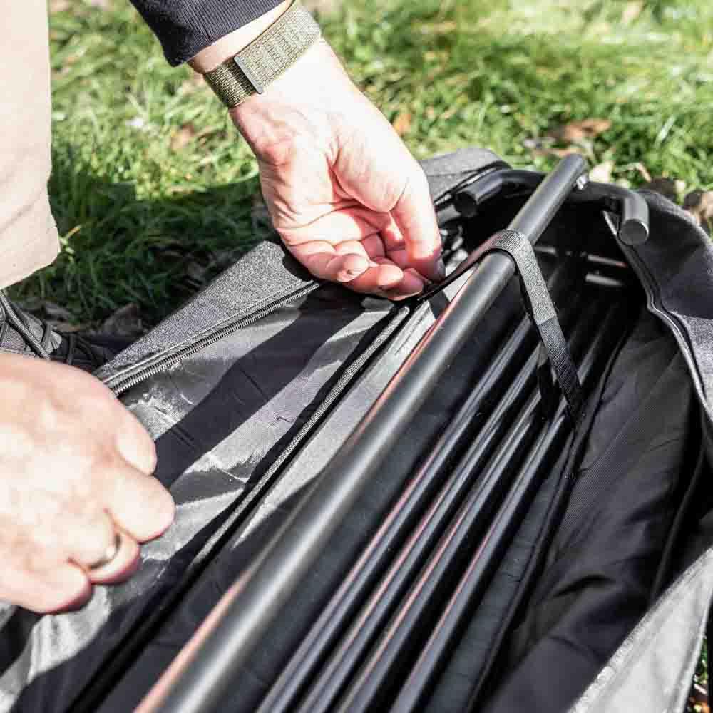 Hands securing black fire bridge poles inside a durable ripstop transport bag with reinforced zipper and strap, designed for farm, garden, camping, and outdoor use.