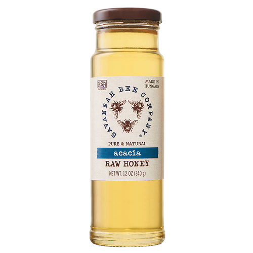 Clear glass jar of golden acacia raw honey with a simple white label featuring bee illustrations, sealed with a brown lid, ideal for kitchen and food pantry use.