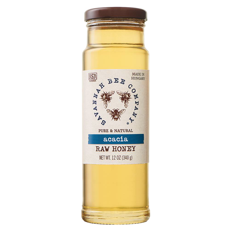 Clear glass jar of golden acacia raw honey with a simple white label featuring bee illustrations, sealed with a brown lid, ideal for kitchen and food pantry use.