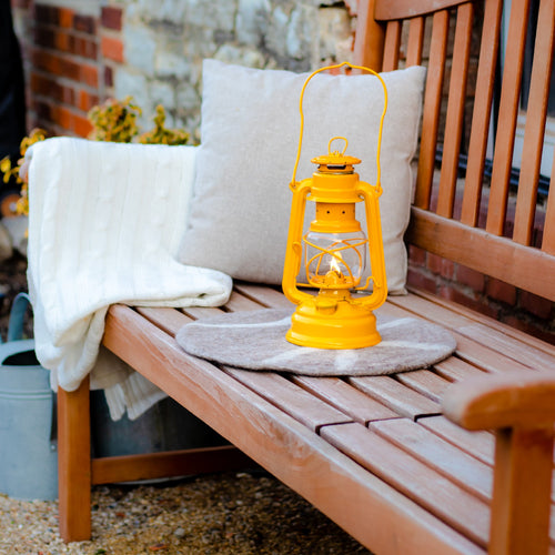 Handcrafted yellow galvanized oil lantern with thermal heat-resistant globe resting on a wooden bench with cozy cushions and blanket, perfect for outdoor, camping, and emergency lighting.