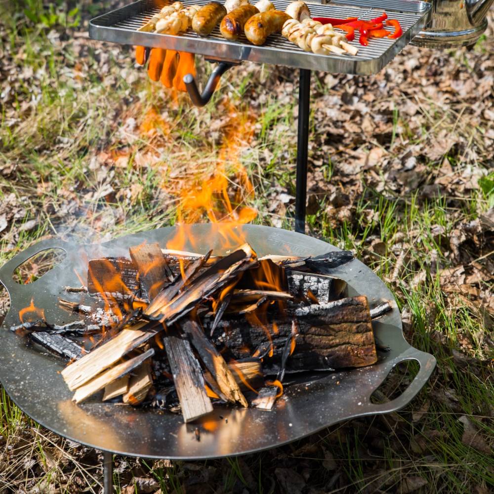 Steel fire bowl with three sturdy legs supporting a grilling rack cooking skewers and sausages over an open campfire, ideal for Farm, Garden & Tool, Camping, Best Sellers, and Promo Eligible collections.