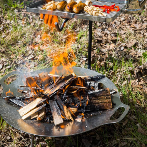 Steel fire bowl with three sturdy legs supporting a grilling rack cooking skewers and sausages over an open campfire, ideal for Farm, Garden & Tool, Camping, Best Sellers, and Promo Eligible collections.