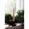 Cordless LED taper candle with realistic flickering amber flame in black holder, sitting on windowsill among holiday greenery and string lights, part of Home & Decor collections.