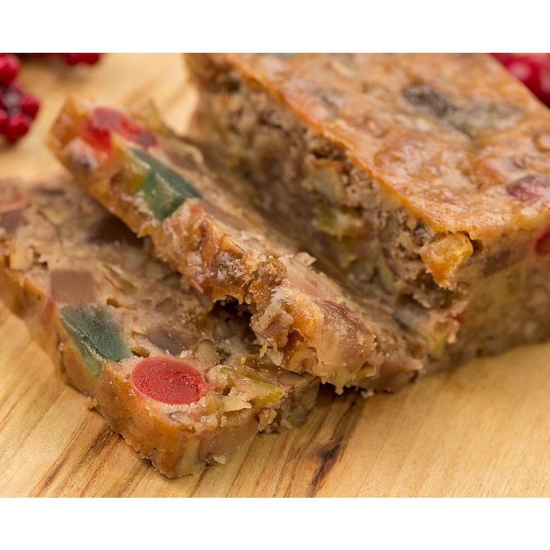 Close-up of handcrafted Christmas fruitcake slice showing abundant nuts and colorful candied fruit pieces, presented on a wooden surface, featured in Kitchen & Food, Snacks and Sweets, USA Made, and Best Sellers collections.