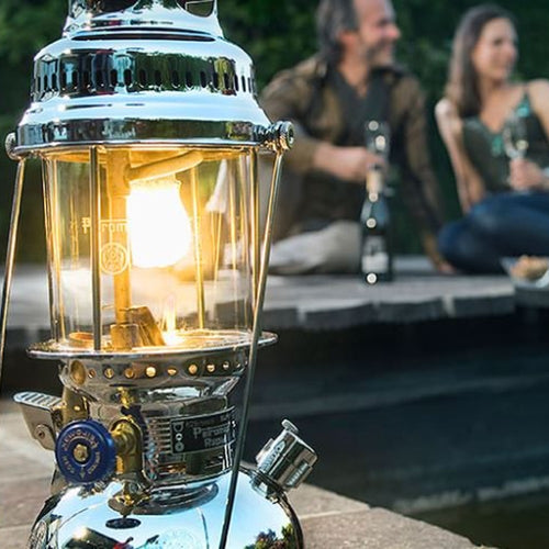Brightly glowing Petromax HK500 kerosene pressure lamp with polished metal finish, providing warm light for outdoor gatherings, camping, and emergency lighting needs.