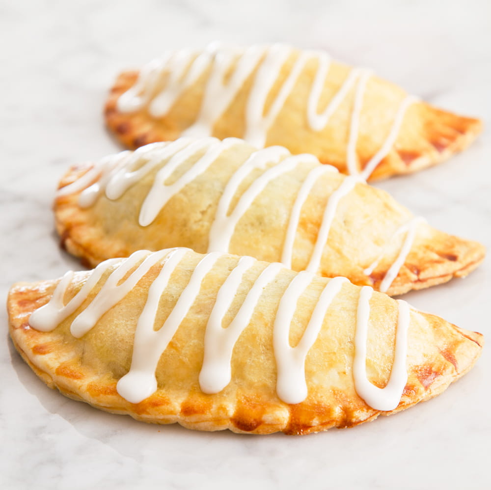 Three golden-brown hand pies with a drizzle of white icing on top, showcasing easy-to-make pastries from Kitchen & Food, Kitchen Gadgets, and Baking Helpers collections.
