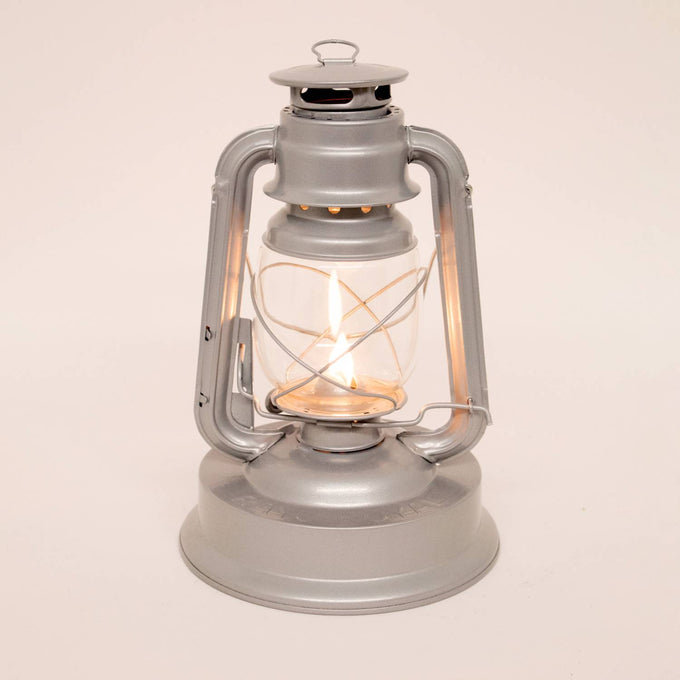 Handcrafted gray metal lantern with glass globe and protective wire frame, burning a bright flame, ideal for farm, garden, camping, emergency supplies, and outdoor use.