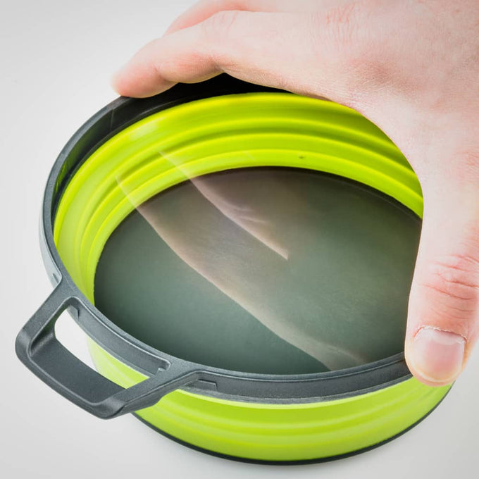 Hand holding a compact collapsible bowl with a translucent secure lid and bright green silicone sides, designed for camping and outdoor use in Farm, Garden & Tool and Best Sellers collections.