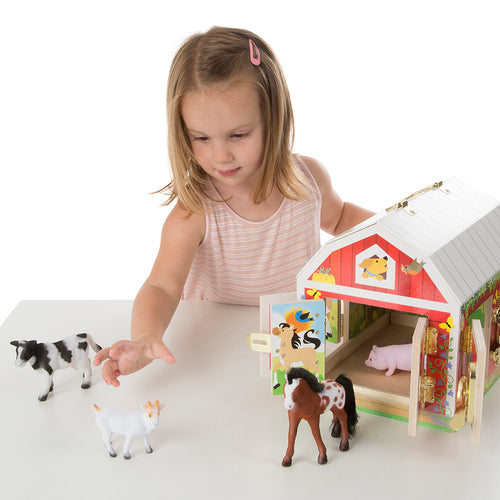 Young child playing with a handcrafted wooden barn toy featuring brass latches, accompanied by four flocked animal figures—a cow, pig, goat, and horse—part of children’s wooden toy collections.