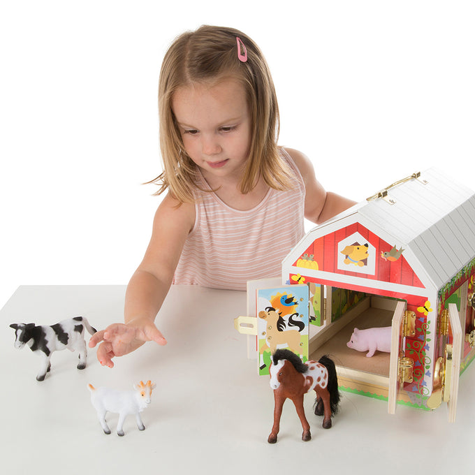 Young child playing with a handcrafted wooden barn toy featuring brass latches, accompanied by four flocked animal figures—a cow, pig, goat, and horse—part of children’s wooden toy collections.