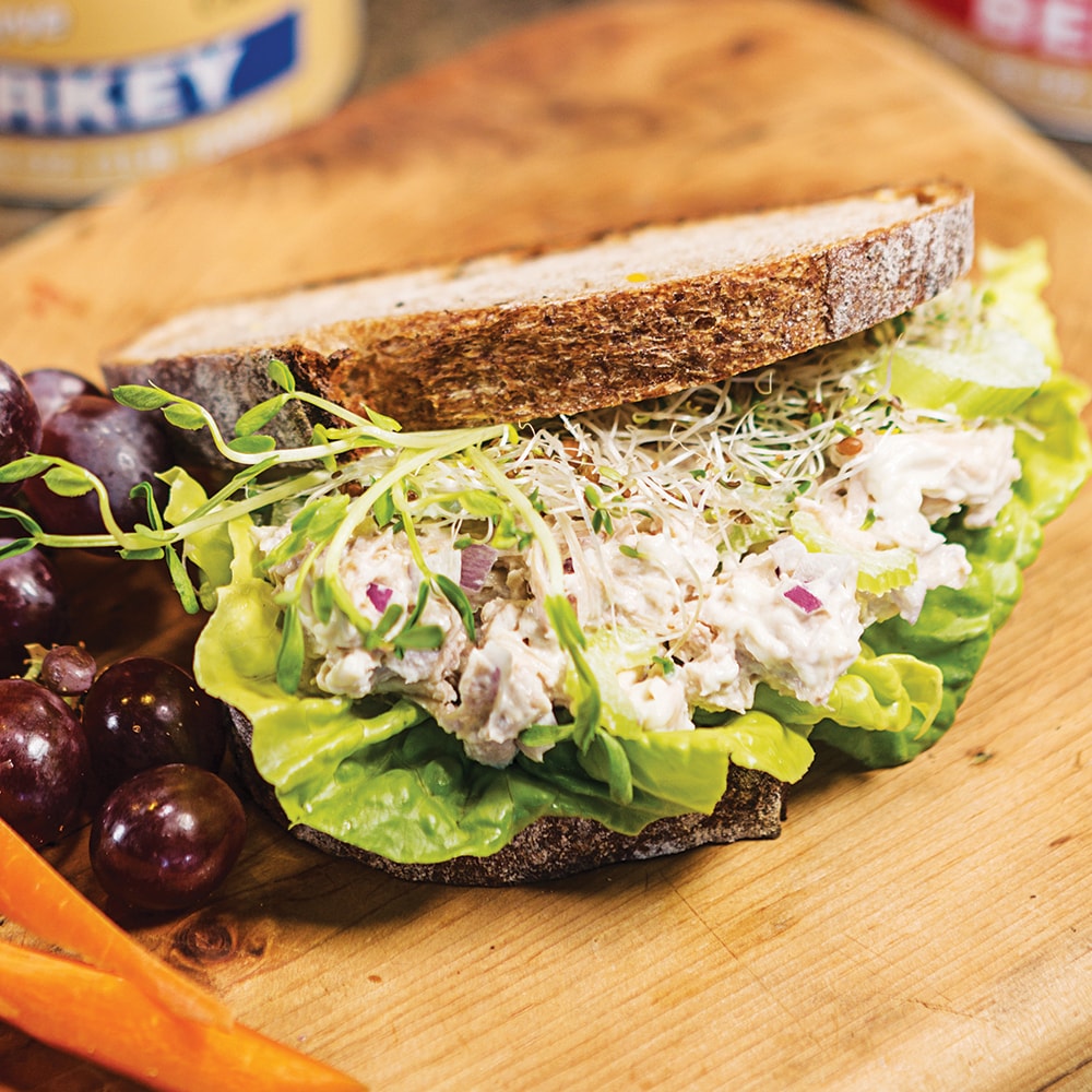 Sandwich featuring creamy chicken salad with chopped red onions, fresh lettuce, and alfalfa sprouts on rustic whole grain bread, served with grapes and carrot sticks, ideal for Kitchen & Food, Food, Meats, Best Sellers, and Promo Eligible collections.