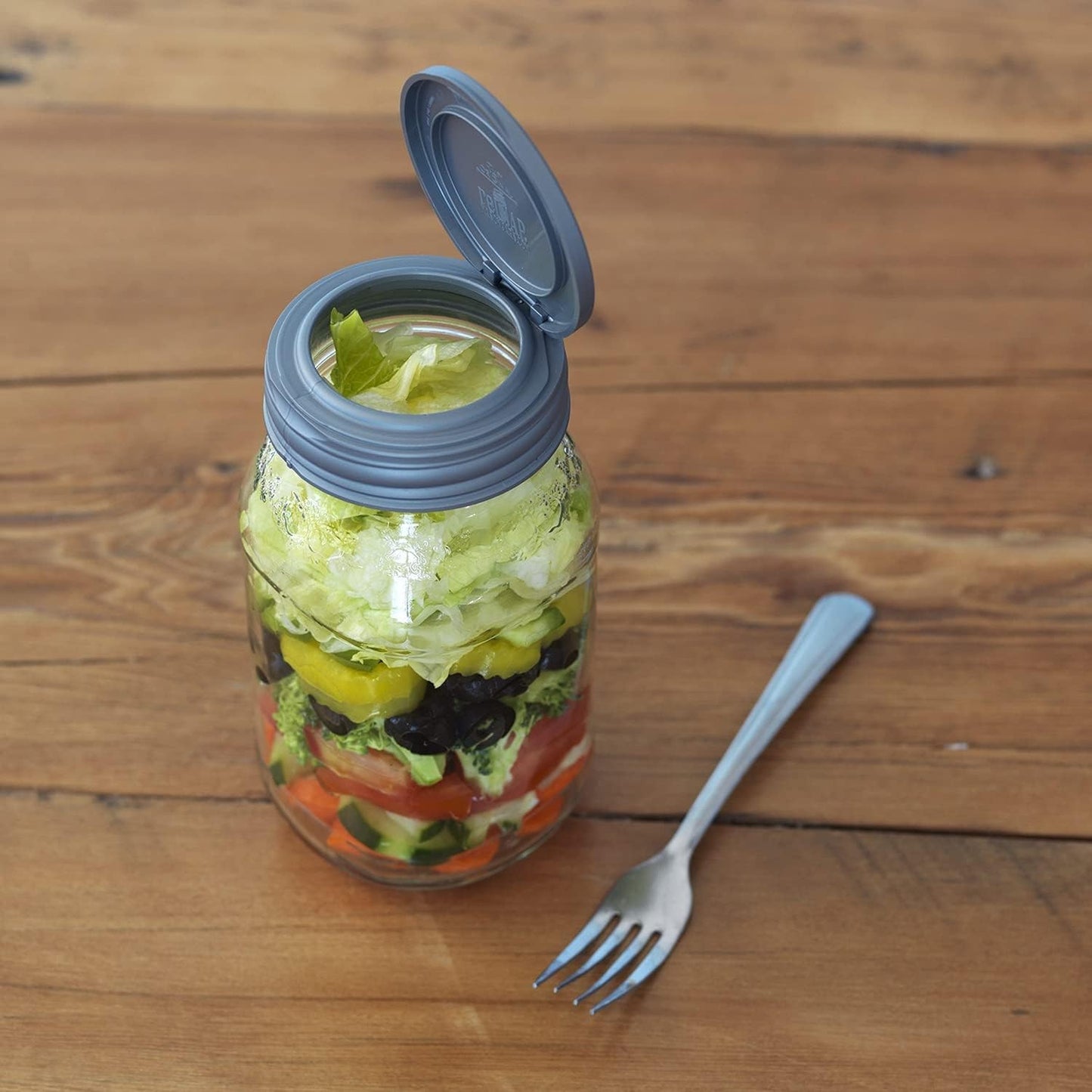 Clear jar with a gray flip top lid open, containing layered fresh salad ingredients, displayed on a wooden surface with a fork, highlighting reusable storage for Home & Decor, Kitchen Gadgets, and Kitchen Accessories collections.