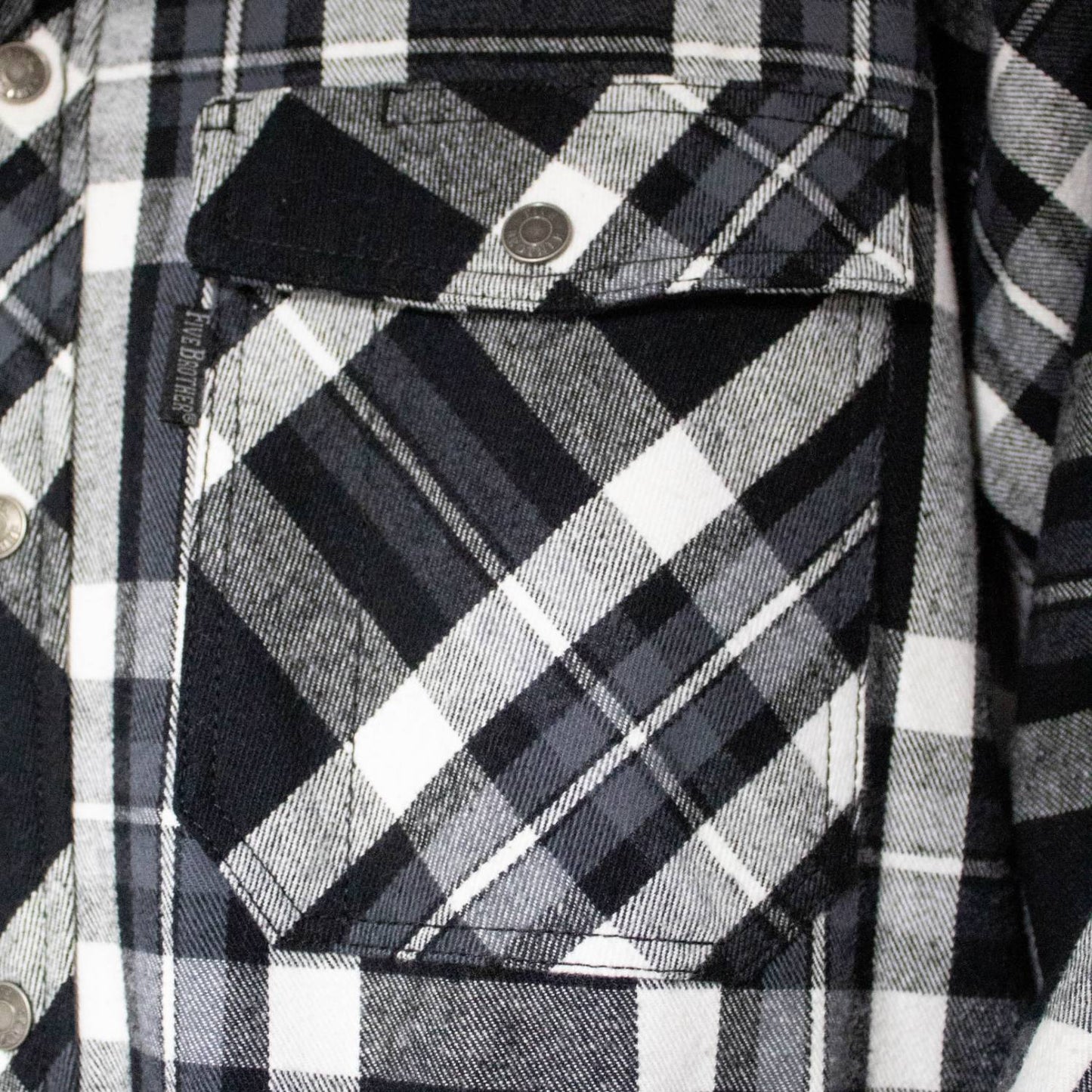 Close-up of a handcrafted black and white plaid flannel jacket pocket featuring detailed stitching and a branded snap button, part of Health & Wellness and Clothing and Accessories collections.