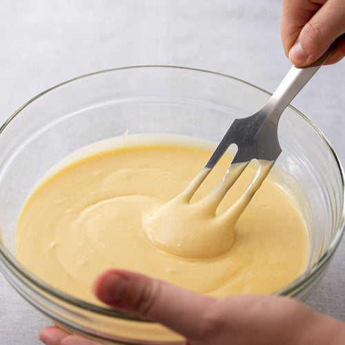 Hand using stainless steel spatula with angled, slotted, sharpened end to mix batter in a clear glass bowl, handcrafted in USA, ideal for Kitchen & Food and Storage and Serving collections.
